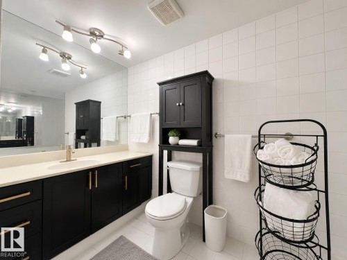 Bathroom featuring a wide vanity with dark cabinetry, light-toned countertop, and a large wall mirror - #301 9808 103 St Nw, Edmonton, AB - Indoor Photo Showing Bathroom