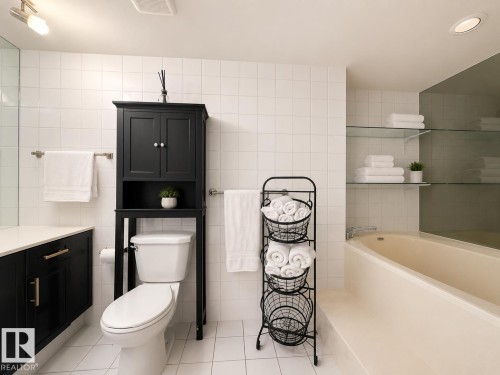 Bathroom featuring white tile flooring and walls, a built-in bathtub, a black vanity with a white countertop, and a black over-the-toilet storage cabinet - #301 9808 103 St Nw, Edmonton, AB - Indoor Photo Showing Bathroom