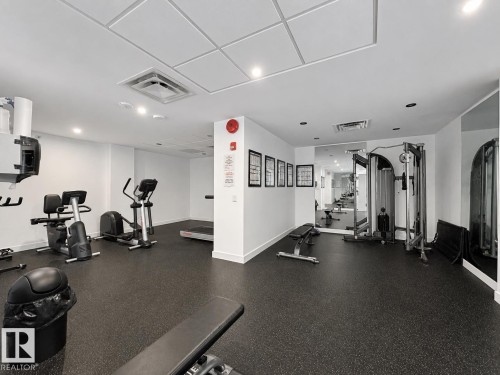 Dedicated fitness room featuring dark rubber flooring, recessed lighting, mirrored walls, and a drop ceiling - #301 9808 103 St Nw, Edmonton, AB - Indoor Photo Showing Gym Room
