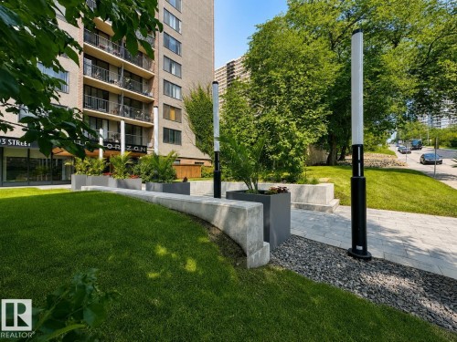 Landscaped grounds featuring a stone-paved walkway, concrete planters, and contemporary outdoor lighting - #301 9808 103 St Nw, Edmonton, AB - Outdoor