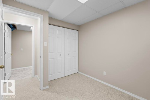 Room featuring light beige wall paint, white bi-fold closet doors, cream-toned carpet flooring, and a white drop ceiling with recessed lighting - 21344 88 Avenue Nw, Edmonton, AB - Indoor Photo Showing Other Room