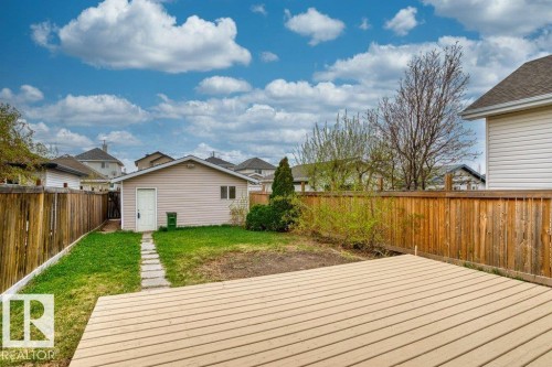 Expansive outdoor deck with wood-finish decking, surrounded by a wooden privacy fence, a detached garage with siding exterior, and a stepping stone path - 21344 88 Avenue Nw, Edmonton, AB - Outdoor