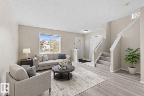 Open-concept living area featuring light wood-finish flooring, a contemporary staircase with white risers and handrails, and a front entry door with decorative glass inserts - 21344 88 Avenue Nw, Edmonton, AB - Indoor Photo Showing Living Room