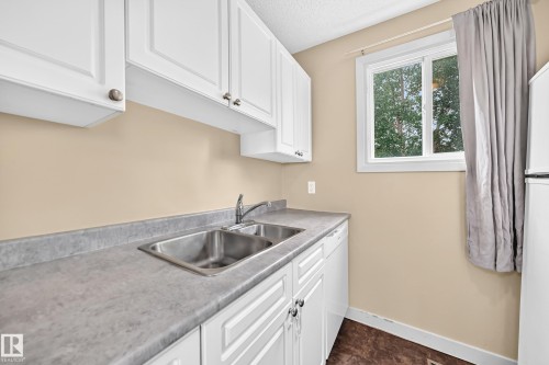White cabinetry, dual basin stainless steel sink, light-toned countertops, and a white-framed window - 6416 180 Street Nw, Edmonton, AB 