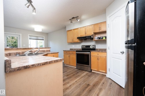 Kitchen featuring wood-finish flooring, stainless steel appliances, wood cabinetry, and a double basin sink with a gooseneck faucet - 1009 Macewan Close Sw, Edmonton, AB - Indoor Photo Showing Kitchen With Double Sink
