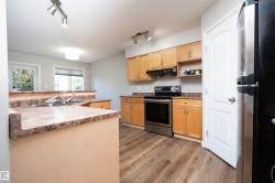 Kitchen featuring wood-finish flooring, stainless steel appliances, wood cabinetry, and a double basin sink with a gooseneck faucet - 