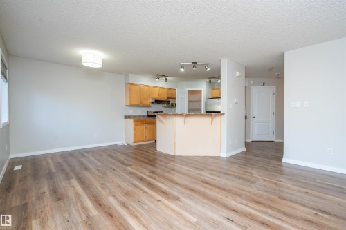 Open-concept living space featuring wood-finish flooring, a kitchen with natural wood cabinetry, stainless steel appliances, and a breakfast bar - 1009 Macewan Close Sw, Edmonton, AB - Indoor Photo Showing Kitchen