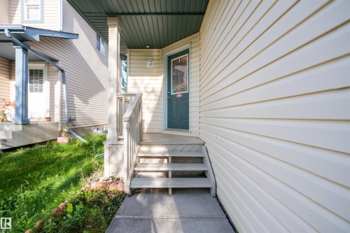 Inviting covered front porch with a dark green entry door, light-colored siding, concrete walkway, and wooden handrails - 1009 Macewan Close Sw, Edmonton, AB - Outdoor