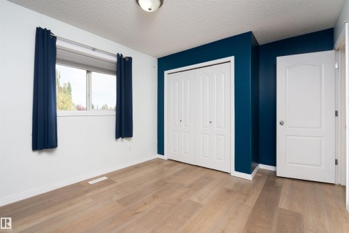 Wood-finish flooring with white baseboards, a window with white trim, and a white bi-fold closet - 1009 Macewan Close Sw, Edmonton, AB - Indoor