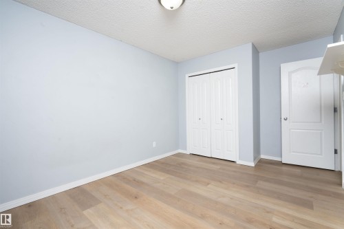 Light wood-finish flooring with white trim, light blue wall paint, and a built-in closet with bi-fold doors - 1009 Macewan Close Sw, Edmonton, AB - Indoor Photo Showing Other Room