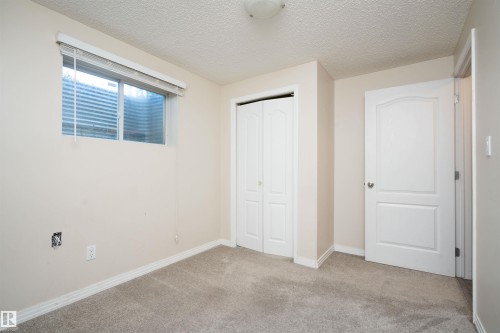 Neutral wall paint, textured ceiling, window with blinds, bi-fold closet doors, and panel-style door - 1009 Macewan Close Sw, Edmonton, AB - Indoor Photo Showing Other Room