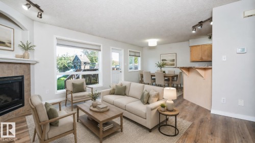Living area featuring a fireplace with a tile surround, large window, and wood-finish flooring - 1009 Macewan Close Sw, Edmonton, AB - Indoor Photo Showing Living Room With Fireplace