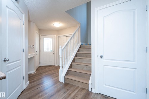 Entry foyer with wood-finish flooring, white spindle staircase, and a front entry door with decorative glass inlay - 1009 Macewan Close Sw, Edmonton, AB - Indoor Photo Showing Other Room