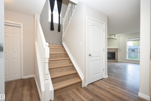 Wood-finish flooring, white paneled doors, staircase with turned newel posts, and a fireplace with tile surround - 1009 Macewan Close Sw, Edmonton, AB - Indoor Photo Showing Other Room