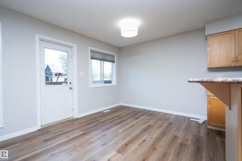 Wood-finish flooring, light gray walls, a flush-mount ceiling light, and light wood cabinetry with a stone-finish countertop - 1009 Macewan Close Sw, Edmonton, AB - Indoor Photo Showing Other Room