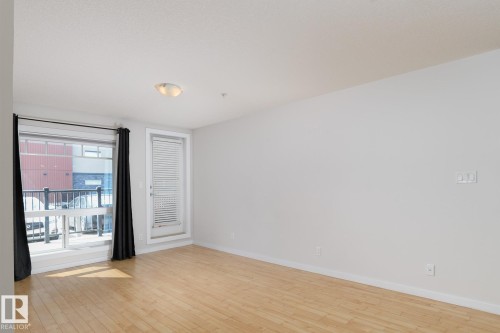 Hardwood flooring, white walls, large window, and flush mount ceiling light - #110 9523 160 Av Nw, Edmonton, AB - Indoor Photo Showing Other Room