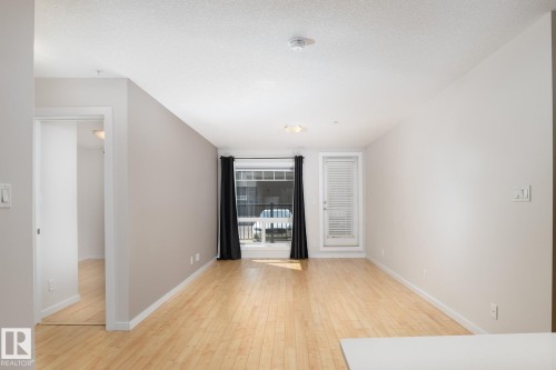 Hardwood-style flooring throughout, light neutral wall colors, and a ceiling-mounted light fixture - #110 9523 160 Av Nw, Edmonton, AB - Indoor Photo Showing Other Room