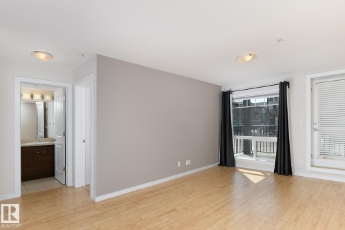 Hardwood flooring throughout, neutral paint palette, and a large window with direct balcony access - #110 9523 160 Av Nw, Edmonton, AB - Indoor Photo Showing Other Room