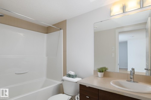 White bathtub with integrated shower, vanity with an undermount sink, and a large wall-mounted mirror - #110 9523 160 Av Nw, Edmonton, AB - Indoor Photo Showing Bathroom