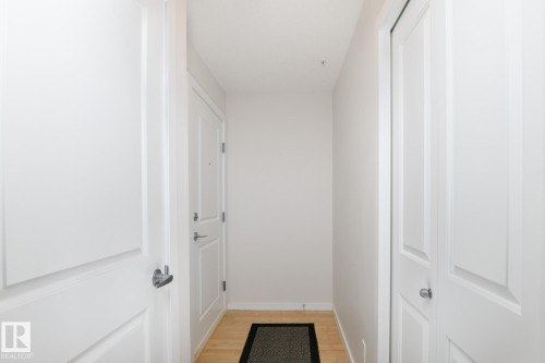Light wood-finish flooring with white wall finishes - #110 9523 160 Av Nw, Edmonton, AB - Indoor Photo Showing Other Room