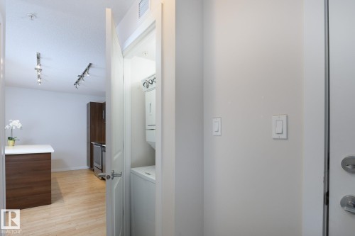 Integrated laundry closet with stacked washer and dryer, wood-finish flooring, and track lighting fixtures - #110 9523 160 Av Nw, Edmonton, AB - Indoor