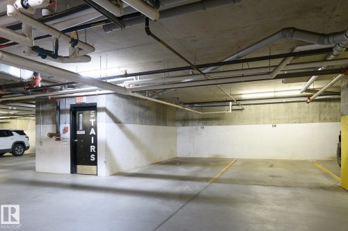 Concrete parking area with painted floor markings and exposed ceiling utilities - #110 9523 160 Av Nw, Edmonton, AB - Indoor Photo Showing Garage