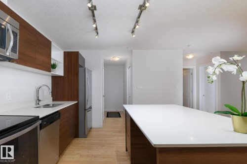 Kitchen featuring wood-finish cabinetry, stainless steel appliances, white countertops, and track lighting - #110 9523 160 Av Nw, Edmonton, AB - Indoor Photo Showing Kitchen With Double Sink