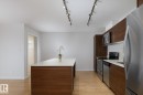 Kitchen featuring wood-finish cabinetry, stainless steel appliances, a white solid surface island, track lighting, and wood-finish flooring - #110 9523 160 Av Nw, Edmonton, AB 
