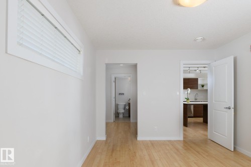 Light wood-finish flooring throughout, white interior doors with contemporary hardware, and a horizontal window with blinds - #110 9523 160 Av Nw, Edmonton, AB - Indoor Photo Showing Other Room