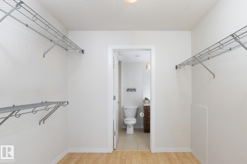 Hardwood-finish flooring with white walls and wire shelving, offering direct access to a bathroom with a neutral-toned tile floor - #110 9523 160 Av Nw, Edmonton, AB - Indoor With Storage