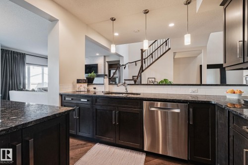 Dark wood-finish cabinetry with silver hardware, stone countertops, stainless steel dishwasher, undermount sink with a gooseneck faucet, and white subway tile backsplash - 1337 Secord Landing Nw, Edmonton, AB - Indoor Photo Showing Kitchen With Upgraded Kitchen