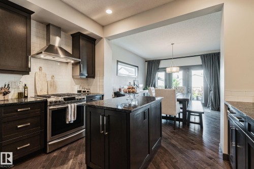 Dark wood-finish cabinetry, stainless steel appliances, dark stone countertops, wood-finish flooring, and a white subway tile backsplash - 1337 Secord Landing Nw, Edmonton, AB - Indoor Photo Showing Kitchen With Upgraded Kitchen