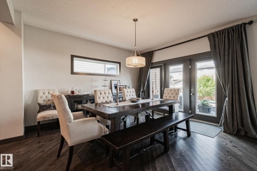 Hardwood flooring, modern pendant light fixture, horizontal accent window, and double French doors to the exterior - 1337 Secord Landing Nw, Edmonton, AB - Indoor Photo Showing Dining Room