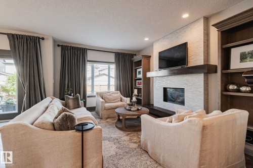 Recessed lighting illuminates the living area with an elegant fireplace featuring a dark wood mantel and a textured tile surround - 1337 Secord Landing Nw, Edmonton, AB - Indoor Photo Showing Living Room With Fireplace
