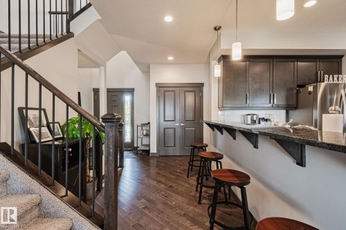 Kitchen bar seating with an integrated breakfast bar, dark wood-finish cabinetry, and stainless steel appliances - 1337 Secord Landing Nw, Edmonton, AB - Indoor Photo Showing Kitchen With Upgraded Kitchen