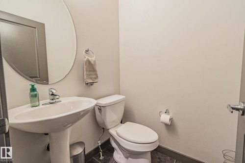 Pedestal sink with chrome faucet, circular wall mirror, and dark tile flooring - 1337 Secord Landing Nw, Edmonton, AB - Indoor Photo Showing Bathroom