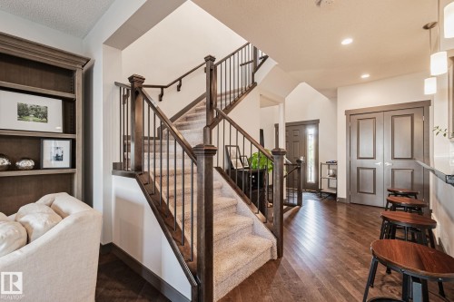 Hardwood-finish flooring, built-in shelving, carpeted staircase with wood newel posts, iron balusters, and a paneled entry door - 1337 Secord Landing Nw, Edmonton, AB - Indoor Photo Showing Other Room
