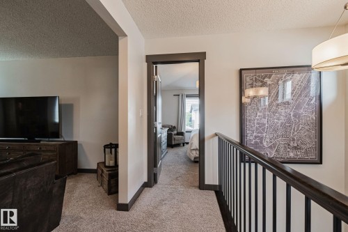 Carpeted hallway with painted trim and railing, leading to a room with window - 1337 Secord Landing Nw, Edmonton, AB - Indoor Photo Showing Other Room