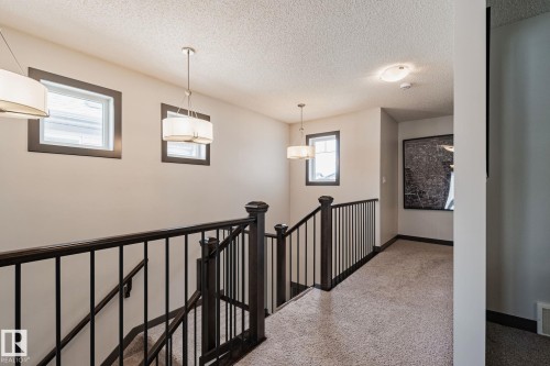 Staircase featuring dark wood newel posts and railings with black metal balusters, complemented by a light-toned carpeted landing and recessed lighting - 1337 Secord Landing Nw, Edmonton, AB - Indoor Photo Showing Other Room