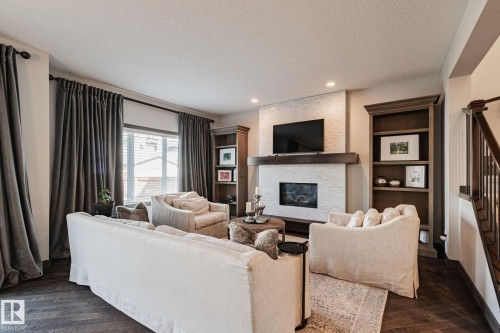 Herringbone wood-finish flooring, built-in shelving, stone-clad fireplace with mantel, recessed lighting, and a prominent window - 1337 Secord Landing Nw, Edmonton, AB - Indoor Photo Showing Living Room With Fireplace