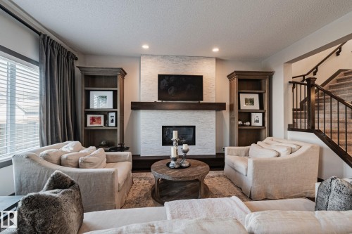 Stacked stone fireplace with a substantial wood mantel, built-in shelving, recessed lighting, and a staircase with wood newel posts and iron balusters - 1337 Secord Landing Nw, Edmonton, AB - Indoor Photo Showing Living Room With Fireplace