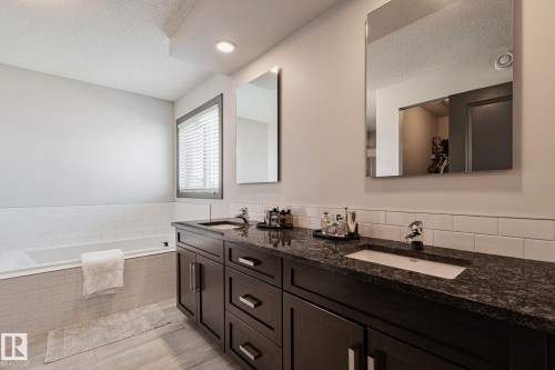 Dual vanity with dark wood-finish cabinetry and stone countertops - 1337 Secord Landing Nw, Edmonton, AB - Indoor Photo Showing Bathroom