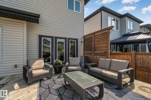 Spacious outdoor deck with light wood-finish planks, dual French doors, a black awning, and a privacy screen - 1337 Secord Landing Nw, Edmonton, AB - Outdoor With Deck Patio Veranda With Exterior