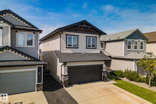Contemporary exterior featuring light-colored siding, black trim accents, a dark shingled roof, a double garage, and a concrete driveway - 1337 Secord Landing Nw, Edmonton, AB - Outdoor With Exterior
