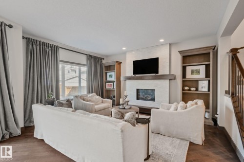 Living area featuring wood-finish flooring, a fireplace with a stone surround and wood mantle, built-in shelving, and recessed lighting - 1337 Secord Landing Nw, Edmonton, AB - Indoor Photo Showing Living Room With Fireplace