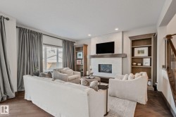 Living area featuring wood-finish flooring, a fireplace with a stone surround and wood mantle, built-in shelving, and recessed lighting - 