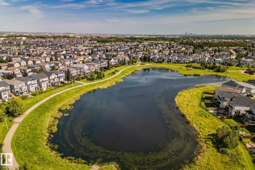 Expansive residential area featuring numerous detached homes, a large body of water, a paved pathway along the water's edge, and extensive green spaces - 1337 Secord Landing Nw, Edmonton, AB - Outdoor With View