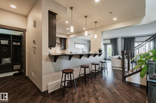 Wood-finish flooring throughout, kitchen with dark wood cabinetry, breakfast bar with pendant lighting, built-in mudroom storage, and an open staircase with dark wood newel post and balusters - 1337 Secord Landing Nw, Edmonton, AB - Indoor