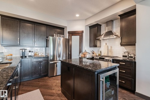 Kitchen featuring dark wood-finish cabinetry, patterned countertops, stainless steel appliances, a tile backsplash, and wood-finish flooring - 1337 Secord Landing Nw, Edmonton, AB - Indoor Photo Showing Kitchen With Stainless Steel Kitchen With Upgraded Kitchen