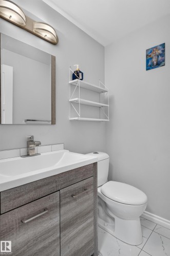White sink with chrome faucet, wood-finish vanity, subway tile backsplash, wall-mounted mirror, and overhead lighting fixture - 8632 184 Street Nw, Edmonton, AB - Indoor Photo Showing Bathroom